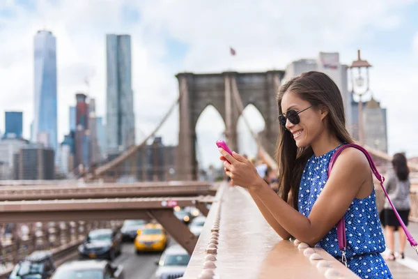 電話だ ニューヨーク市の女性はマンハッタンのスカイラインでブルックリン橋を歩く電話アプリを使用しています 米国ニューヨーク市サングラスを身に着けている若い女性の専門多文化女性 — ストック写真