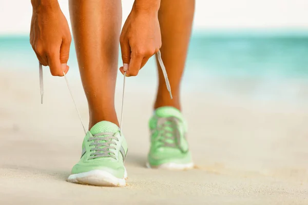 ランニングフィットランナーの女性がジョギングやビーチの靴レースを結ぶ上を歩く準備を実行します 朝のビーチでのランニングシューズ 夏の外での早期トレーニング — ストック写真