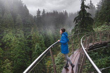 Canada Autumn travel destination in British Columbia. Asian tourist woman walking in famous attraction Capilano Suspension Bridge Park in North Vancouver, canadian vacation for tourism. clipart