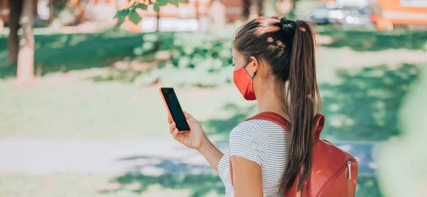大学生们戴着面具和背包 在大学的虚拟课堂上使用手机应用程序 回到学校 女学生拿着手机在校园里站在横幅后面学习 — 图库照片