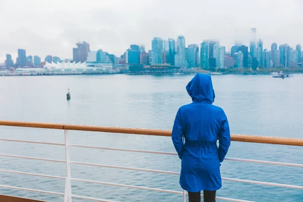 Autumn city scenery woman walking alone under the rain wearing blue raincoat in wet cold day. Skyline of Vancouver, Canada. Cruise ship travel destination.