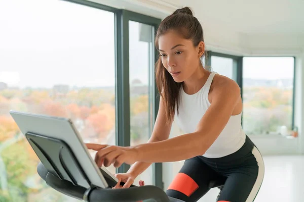 ホームフィットネスワークアウトスマート固定自転車室内での女性のトレーニング自転車の練習のためのライブストリーミングサブスクリプションサービスにオンラインで接続画面を見て 若いアジアの女性アスリート — ストック写真