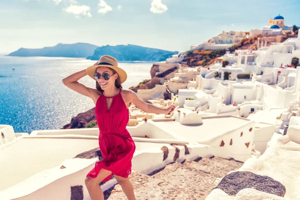 ヨーロッパ旅行の楽しみ 女性の観光客は サントリーニ島の豪華な休日の目的地で喜びの実行 ギリシャでの夏休みのクルーズ アジアの女の子で赤ドレスと帽子とともにギリシャの白い家の背景 — ストック写真