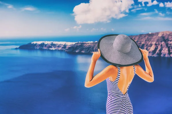 Luxury travel vacation Europe destination woman. Elegant lady in hat and dress in Santorini , Greece. Tourist relaxing living fancy jet-set lifestyle on cruise holidays. View of sea and Caldera.