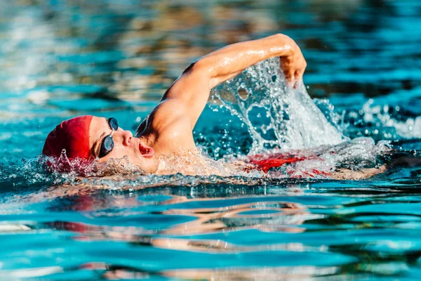 青い水の屋外プールで男性の水泳クロールフリースタイル 運動選手の若い男の肖像は赤いキャップを着てクロールを泳いでゴーグルを泳ぐ トライアスロンのためのトライアスロントレーニング — ストック写真