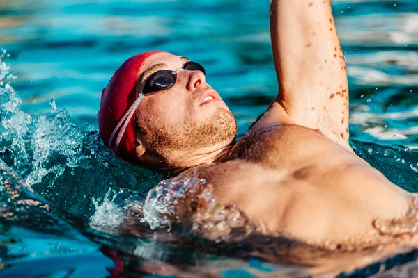 男人游回来爬行 男子游泳运动员穿着泳镜和泳帽 在游泳池里爬行仰泳 健身和健康的生活方式 — 图库照片