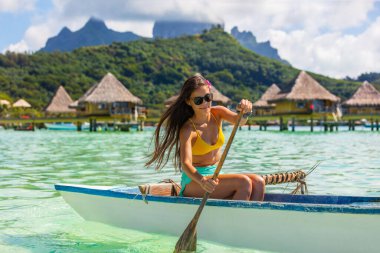 Outrigger Canoe - woman paddling in traditional French Polynesian Outrigger Canoe for recreation sport watersport competition. Bora Bora with Mount Otemanu and overwater bungalow resort hotel. clipart