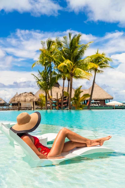 夏休みを楽しむラウンジチェアでリラックスした豪華なホテルスイミングプールの女性 ウォーターラウンジャーで帽子と赤い水着で観光客 — ストック写真
