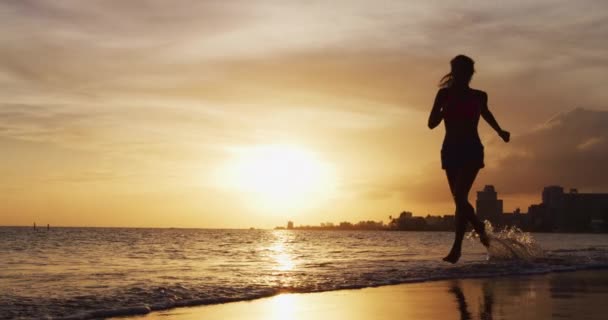 在夕阳西下的沙滩上跑步的女运动员 健美跑步的女孩夏天在大海边的美丽落日或日出中训练全身而退 慢动作 — 图库视频影像