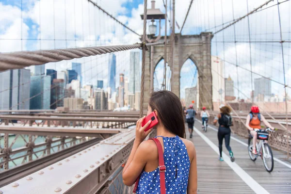 ニューヨークの観光客の女性は マンハッタンのスカイラインに向かって象徴的なブルックリン橋を歩いて電話で話しています 若い女性のプロフェッショナル多文化女性 ニューヨーク市 アメリカ — ストック写真