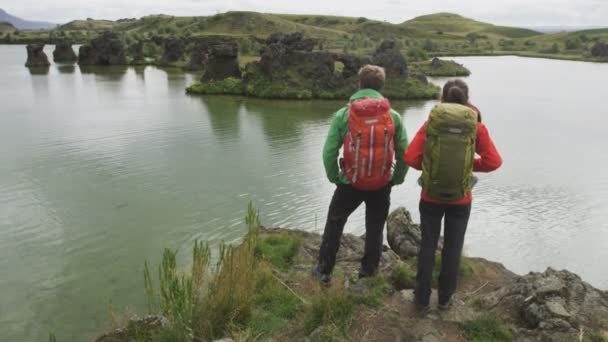 ビューを見て旅行やハイキングのカップル 美しい自然景観の中でバックパックトレッキングを着て湖の外でハイキング中の人々 アイスランド ミヴァトン湖の健康的な生活を送るアクティブな若いカップル — ストック動画