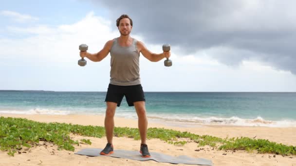 健美的男子在海滩上举哑铃 做肩哑铃侧举练习 锻炼在海滩锻炼的男性健身模型 实际时间 — 图库视频影像