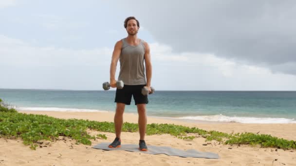 健身男子在沙滩上举起哑铃 进行前哑铃升起 即交替前提高肩部的运动能力 锻炼在海滩锻炼的男性健身模型 实际时间 — 图库视频影像