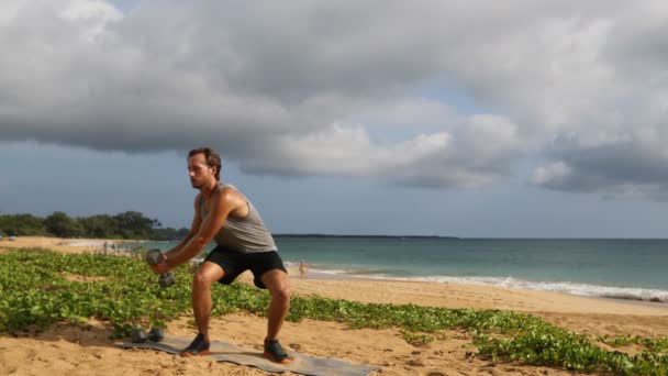 フィットネス運動 男はダンベルでツイスティングウッドチョップ運動を行います ダンベルを使用してビーチでフィットネスワークアウトを行うフィットネスモデルをフィット — ストック動画