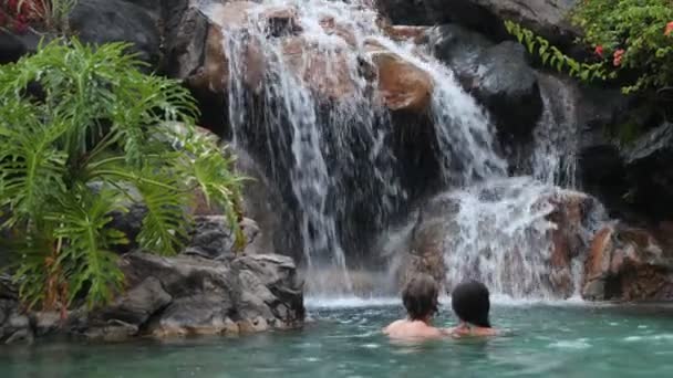 在天堂度假 一对年轻夫妇正在旅行 看着美丽的瀑布 多民族妇女和男子正在享受假期 有爱心的男人和女人都在瀑布下的水池里 — 图库视频影像