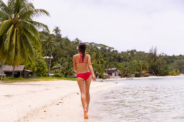 海滩漫步宁静 穿着红色比基尼的女人在法属波利尼西亚塔希提岛波拉波拉海滩散步 这个图像完全没有修饰 模型没有化妆 原始图像 图库照片