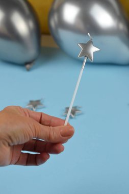 A hand holding a silver star-shaped candle against a light blue background with silver balloons and matching candles in the frame. Perfect for celebrations, parties, or festive themes with a modern touch. clipart