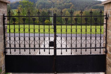 Close huge cemetery gate with outlook outside into the village street and hill and forest, conceptual photo of life and death clipart