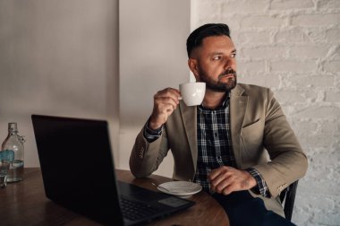Bir kafede kahve içerken bilgisayarında çalışan yakışıklı bir iş adamı.