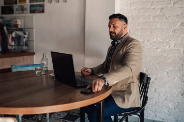 Akıllı telefon kullanan yakışıklı bir iş adamı ve bir kafede kahve içerken dizüstü bilgisayarı üzerinde çalışıyor.