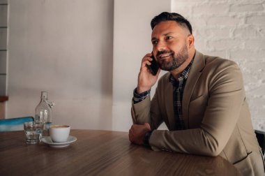 Kafede kahve içerken akıllı telefon kullanan yakışıklı bir işadamı.