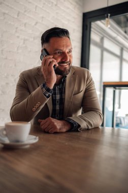 Kafede kahve içerken akıllı telefon kullanan yakışıklı bir işadamı.