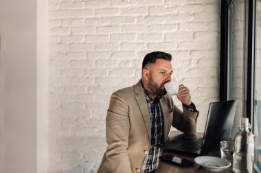 Bir kafede kahve içerken bilgisayarında çalışan yakışıklı bir iş adamı.