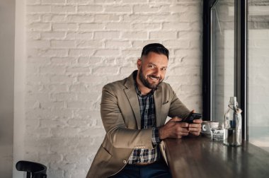 Kafede kahve içerken akıllı telefon kullanan yakışıklı bir işadamı.
