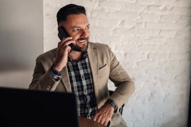 Akıllı telefon kullanan yakışıklı bir iş adamı ve bir kafede kahve içerken dizüstü bilgisayarı üzerinde çalışıyor.