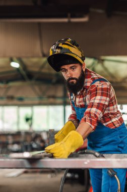 Genç beyaz adam ölçümler yaparak ve metali öğütmek için noktaları işaretleyerek üretim için malzeme hazırlıyor. Makine ve aletlerle dolu kapalı bir tesiste çok çalışmak..