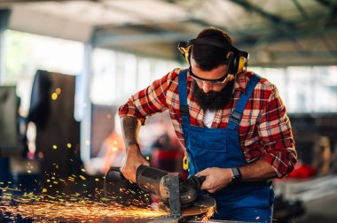 Kendini işine adamış işçiler öğütücüsünü metal plakayı keserken ve metal bir yapı yaratırken kullanıyorlar. Tehlikeli bir ortamda çalışırken iş tulumu ve güvenlik gözlüğü takmak. Boşluğu kopyala.