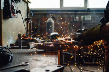 Altın kıvılcımlar her yöne uçarken metal plakayı öğüten öğütme makinesine odaklan. Endüstriyel tesislerdeki elektrikli aletlerle çalışıyor. Açı öğütücüyle metal işleme.
