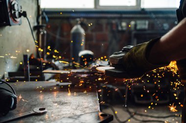 Kıvılcımlar dört bir yana uçuşurken öğütme makinesi iş başında. Adamın elleri koruyucu eldiven giyerken öğütücüyü tutuyor. Metal endüstrisinde çalışırken dikkat çekmek. Boşluğu kopyala.