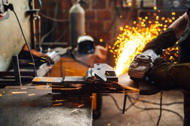 Kıvılcımlar dört bir yana uçuşurken öğütme makinesi iş başında. Adamın elleri koruyucu eldiven giyerken öğütücüyü tutuyor. Metal endüstrisinde çalışırken dikkat çekmek. Boşluğu kopyala.