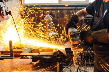 Çalışan yüzeyde altın kıvılcımlar uçuşurken bir profesyonel metal plakayı dikkatlice öğütüyor. Metal endüstrisinde elektrikli bir aletle çalışmak. Tehlikeli iş konsepti. Boşluğu kopyala