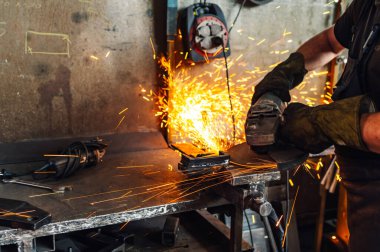 Profesyonel işçi, metal bir inşaat parçasını şekillendirirken öğütme makinesi kullanıyor. Bulanık zeminde altın kıvılcımlar yağıyor. Tehlikeli bir ortamda metal parçaları kaynıyor. Boşluğu kopyala.