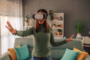 Evde sanal gerçekliğin sanal gerçeklik gözlüklerini kullanırken ve uzayı keşfederken elleriyle el kol hareketi yaparken mutlu ve mutlu bir kadının deneyim kazanması. Modern teknoloji eğlence kavramı.