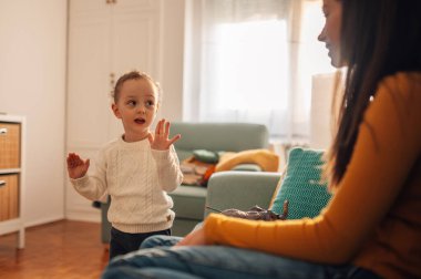 Geveze küçük bir çocuk sıcak bir evde birlikte vakit geçirirken annesiyle konuşuyor. Küçük bir çocuk, rahat evinde eğlenirken annesiyle konuşuyor..