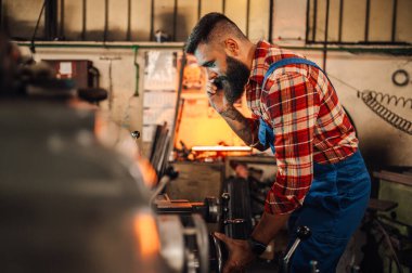 Metal iş makinesinin önünde telefonla konuşan tecrübesiz bir metalürji çalışanı tamir etmek ya da kurmak için talimat alıyor. Bir işçi çalışırken atölyesinde akıllı telefon kullanıyor..