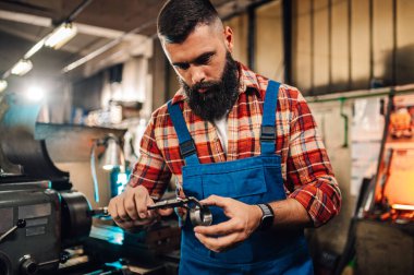 Metalürjist, kalibre ile yaptığı metal kesiği ölçüyor. Mavi yakalı bir işçi ağır metal endüstrisi fabrikasında metal parçaları ölçerken bir aletle çalışıyor..