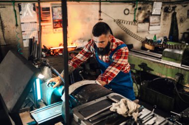 Torna makinesinin ve bir metalürjistin üst görüntüsü. Bir rulo kesim, sıkıcı, tamir, onarım. Arka planda ışıklar var. Temiz saç, kırmızı ekose gömlek ve mavi tulum..