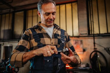 Kıdemli gri saçlı metal çevirici, metal mühendisi, kalibre ile metal halkayı kontrol ediyor. İç çapı. Metal montaj, metal rulo kesim, makine elementi. Ekose gömlek ve tulum..