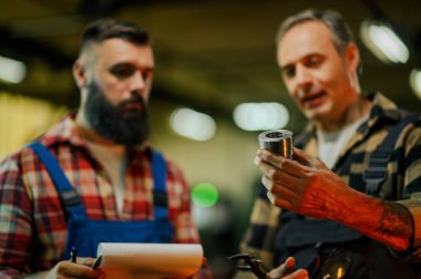 Silindir makine elemanı ya da arka planda bulanık bir denetleyicisi olan uygun, vites parçası tutan bir tamircinin eline seçici odaklan. Genç adam elinde bir dosya tutuyor. Atölye ayarları.