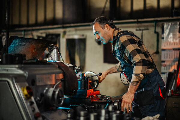 A grey haired machine expert checking out a machine in a factory setting. Fixing, repairing the equipment. Various knobs and leavers. A focused professional machinist is using metal processing machine