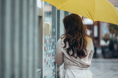 ATM makinesini kullanırken elinde sarı bir şemsiye tutan güzel bir genç kadın.