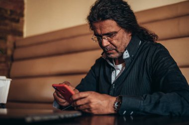 Bir kafede çalışırken akıllı telefon ve dizüstü bilgisayar kullanan kıdemli İspanyol Kübalı adamlar.