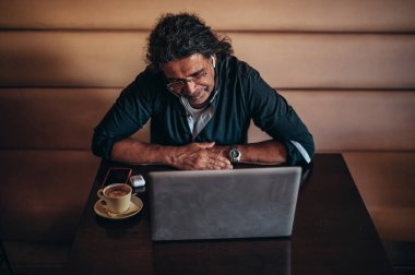 Üst düzey İspanyol Kübalı adamlar bir kafedeyken online toplantı için dizüstü bilgisayar kullanıyorlar.