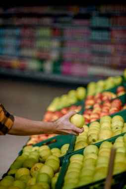 Süpermarkette genç yakışıklı bir adam market alışverişi yaparken ürün seçiyor ve alışveriş arabası tutuyor.