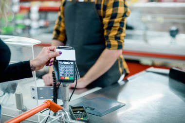 Bir kadın elinin, kredi kartıyla bir süpermarkette, nakit redüksiyoncusu üzerinden temassız ödeme yaparken yakın plan çekimleri.