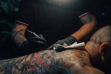 Koyu renk bir dövme stüdyosunda çalışırken erkek derisine dövme yapan profesyonel bir dövme sanatçısı. Dövme yaptırıyorum. Sanat ve tasarım kavramı.